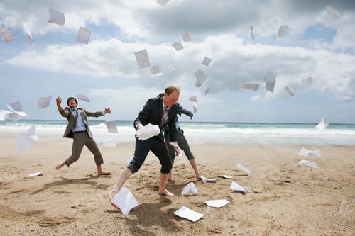 Preview: Businessmen tossing papers away at beach