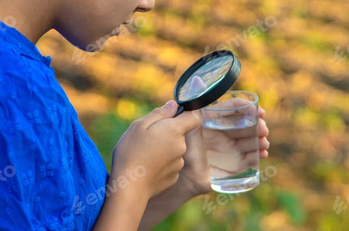 Preview: A child looks at water through a magnifying glass. Selective focus.