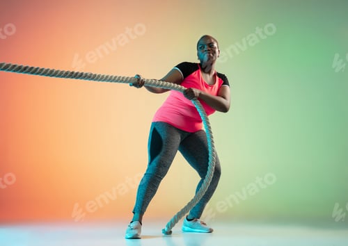 Preview: Young african-american plus size female model's training on gradient background