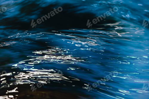 Preview: Abstract close up of flowing river water with light reflections on the surface.