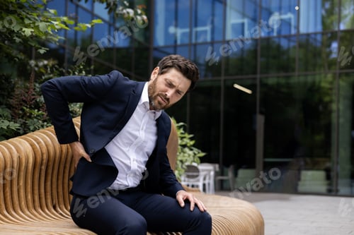 Preview: A young businessman man in a suit sits outside an office center and a bench and holds his hand