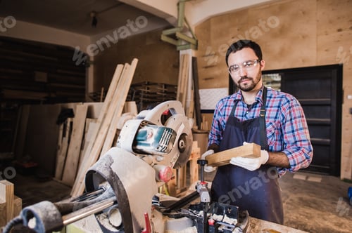 Preview: Young craftsman in uniform working at carpentry and looking to camera