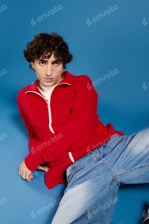 Preview: Stylish young man showcases modern fashion against vibrant blue background with confidence