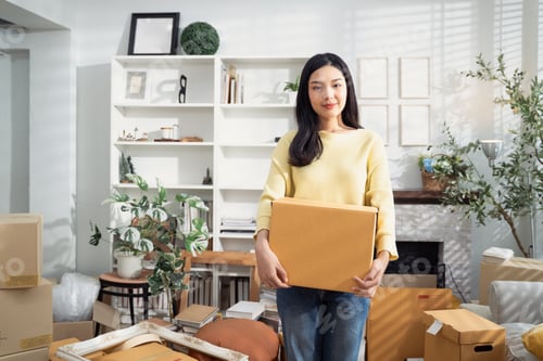 Preview: Asian woman holding cardboard box after packing stuff for moving house