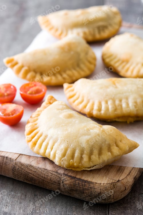 Preview: Delicious homemade empanadas with cherry tomatoes resting on wooden cutting board