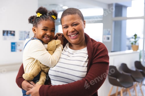 Preview: Portrait of happy african american mother and daughter in waiting room at hospital