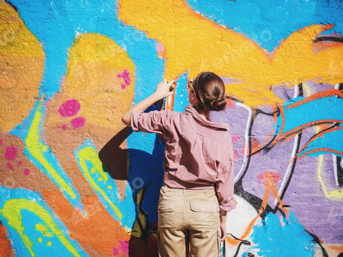 Preview: Beautiful Young Girl making a colorful graffiti with aerosol spray on urban street wall.