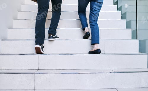 Preview: Rearview shot of two unrecognisable businesspeople walking up a staircase together in an office