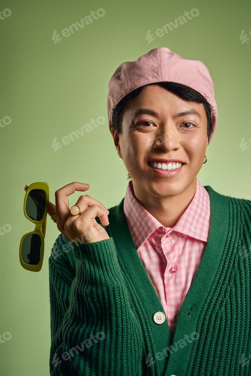 Preview: Stylish Asian man poses in green studio wearing pink checkered shirt with cardigan