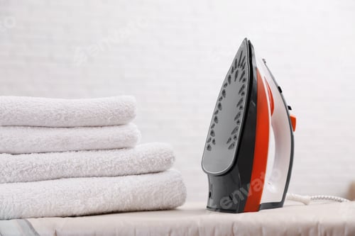 Vista previa: New modern iron and clean towels on board against light background. Laundry day