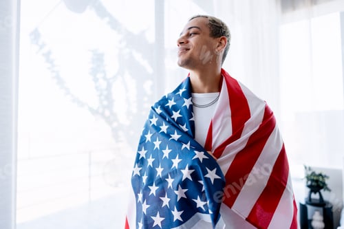 Preview: Young man proudly displaying United States flag against bright window background
