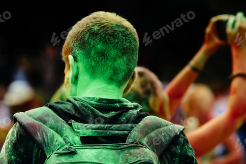 Preview: back of hipster man all in colorful powder at holi fest, festival of colors in summer