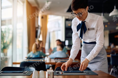 Preview: Hotel waitress setting dining tables in a restaurant.