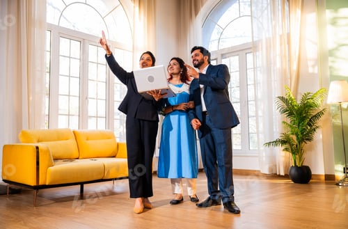 Preview: Discussing layout, Indian woman real estate agent with young married couple walking in property.