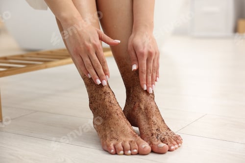 Preview: Woman applying body scrub onto her feet indoors, closeup