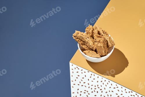 Preview: Bowl of crunchy peanut brittle on yellow and blue geometric surface with seed