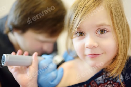 Preview: A caring doctor checks moles on the skin of a small child. A dermatologist looks using dermatoscope