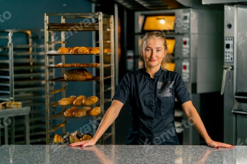 Preview: girl baker in a bakery against the background of ovens and a variety of fresh pastries