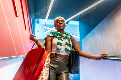 Preview: Stylish african woman coming down an escalator carrying shopping bags
