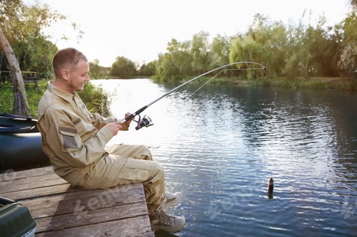 Preview: Man with rod fishing on wooden pier at riverside. Recreational activity