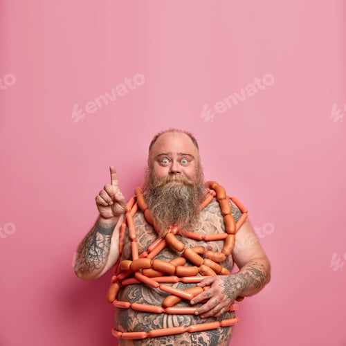 Preview: Food, obesity, overeating concept. Tattooed bearded fatso male wrapped by sausages, points finger ab