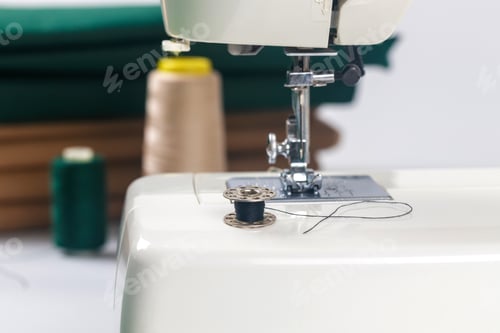 Preview: Sewing machine with black thread and spools on table in crafting space during daylight