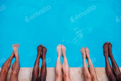 Preview: Young people lying near swimming pool. Cropped image of legs over blue water
