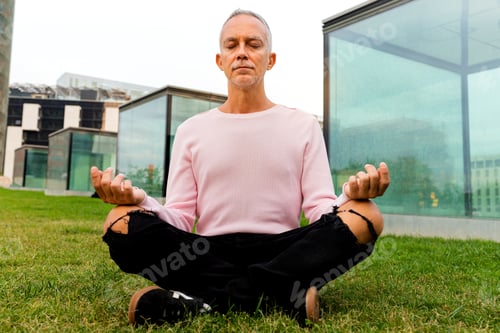 Preview: Caucasian adult man wearing pink sweater meditating in city public park.