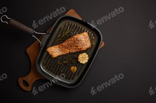 Preview: top view of arranged grilled salmon steak with rosemary on wooden cutting board on black tabletop