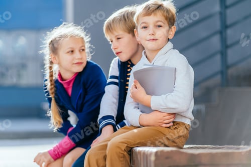 Preview: Portrait of three little children with book sitting on the bench in the schoolyard at the day time,