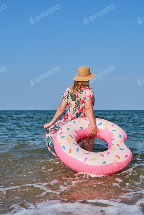 Preview: Woman in hat and bikini swimming on inflatable donut ring