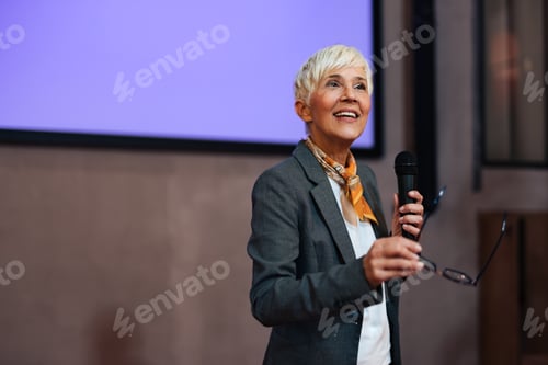 Preview: Smiling woman speaking to an audience at a conference, standing at the projection screen.