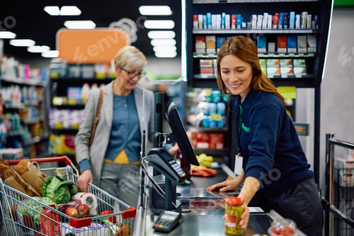 Preview: Happy cashier scanning goods while working at supermarket.