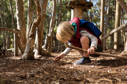 Preview: Little girl with backpack holding stick in her hand playing with rock