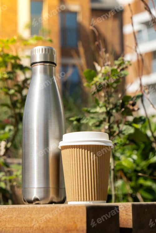 Preview: Reusable steel thermo water bottle on wooden bench with paper cup. Sustainable lifestyle. Plastic