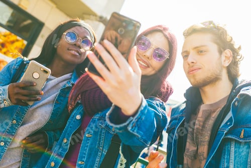 Preview: Multiracial friends taking selfie outdoors. Happy friendship concept with young students having fun.