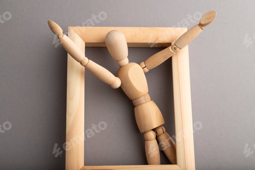 Preview: Wooden mannequin climbs out of a wooden frame with raised arms on gray pastel background
