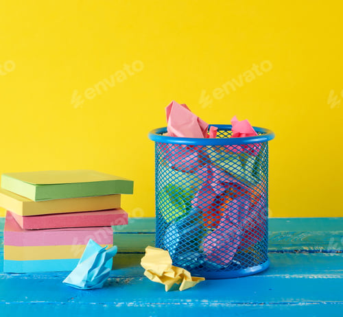 Preview: Blue metal bucket filled with crumpled multi-colored white paper, yellow background