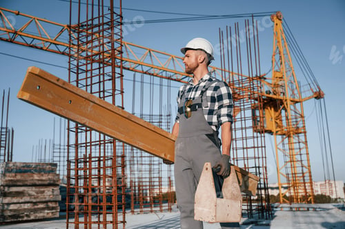 Preview: With big wooden plank in hand. Man is working on the construction site at daytime