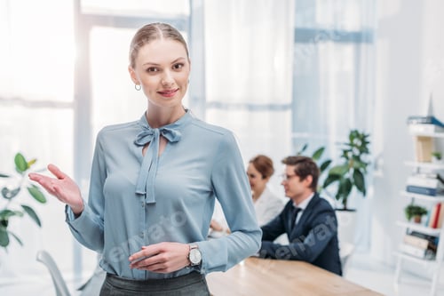 Preview: beautiful recruiter gesturing while standing near coworkers in office