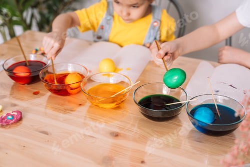 Preview: Children paint eggs for Easter in glass plates with paint on wooden table