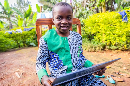Preview: Happy African child sitting on a chair and holding his tablet. Education concept