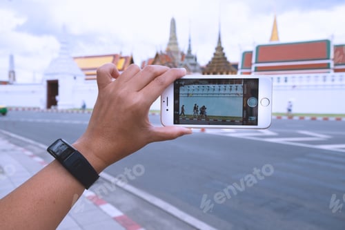 Preview: Traveling in Bangkok. A female hand holding a smart phone while taking picture of the Grand Palace.
