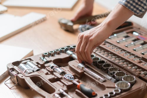 Preview: young man choobsing wrench from the tool kit on the wooden floor