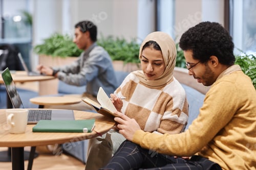 Preview: Middle Eastern woman in office and looking at notes with male colleague