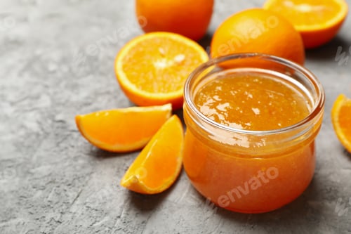 Preview: Oranges and glass jar with jam on gray background, close up