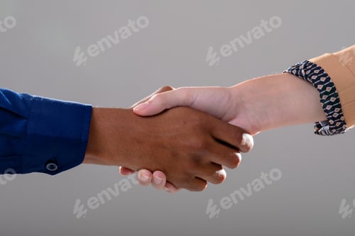 Preview: Midsection of caucasian and african american business people shaking hands on grey background