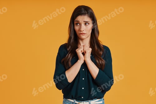Preview: Surprised young woman in casual clothing making a face while standing against yellow background
