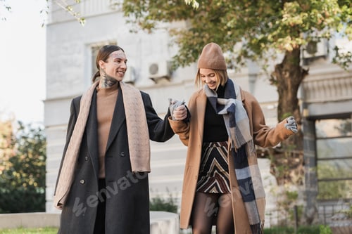 Preview: smiling blonde woman in coat and hat holding hands with tattooed boyfriend during date