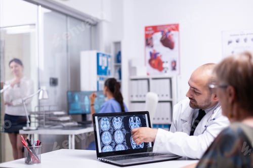 Preview: Doctor pointing on digital cerebral x-ray talking with senior woman